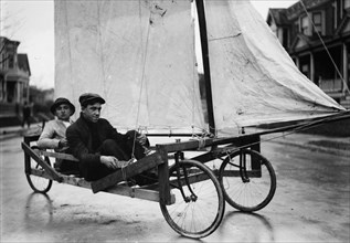 Two young adults having fun riding in a sail wagon or sail cart riding down a street in Brooklyn, possibly Victorian Flatbush ca. 1912
