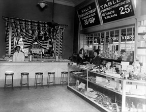 Interior of People's Drug Store, 14th and Park Streets, Washington, D.C., with employee behind soda fountain and another employee behind counter with product display ca. 1921-1923