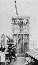 Assemblage of the Statue of Liberty in Paris, showing the bottom half of the statue erect under scaffolding, the head and torch at its feet ca. 1883
