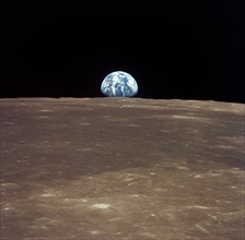 (16-24 July 1969) This view from the Apollo 11 spacecraft shows Earth rising above the moon's horizon. The lunar terrain pictured is in the area of Smyth's Sea on the nearside