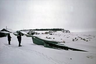 Men looking out at boats on the Elim Alaska coastline ca. March 1974