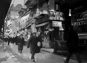 Date: 1910-1915 - Men walking on sidewalk in the Bowery, New York City 1910s