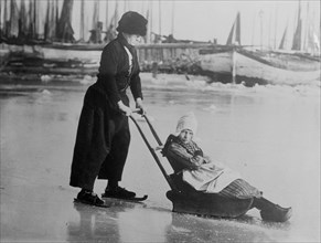 In Holland, woman pushing child on frozen lake, looks very unhappy, ca. 1914