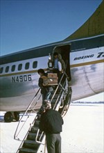 Carl Huntington and his wife exit a Wien Consolodiated airplane at Galena, Alaska, Carl is holding his trophy from winning the 1974 Iditarod Race ca. March 1974