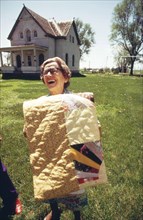 Mrs. John Bettger, president of the Fairmont Golden Circle Senior Citizens Club, on lawn of Fairmont's oldest house. Mrs. Bettger holds a quilt made by members of the club, May 1973