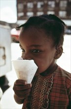 1973 -Black Ghetto Child Savors A Snow Cone Just Received From A Sidewalk Vendor On Chicago's West Side, 06/1973