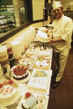 German Immigrant Hans Strzyso Is the Chief Baker at Madsens Supermarket. He Specializes in All Types of Decorated Cakes and Ethnic German Baked Goods Which Are Made Fresh Daily ca. 1975