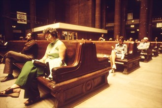 Passengers sit on massive wooden benches which fit in with the architecture of the cavernous Chicago Union Station, June 1974