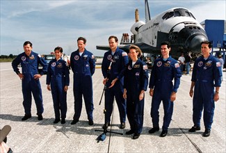 With the Space Shuttle Orbiter Columbia in the background, STS-83 Mission Commander James D. Halsell (center) gives a post-landing briefing on Runway 33 at KSC’s Shuttle Landing Facility ca. 1997