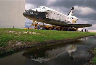 The Space Shuttle Orbiter Columbia is reflected in a nearby pond as it rolls over to the Vehicle Assembly Building (VAB) ca. 1997