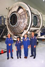 Members of the STS-88 crew pose with the Node 1 of the International Space Station in the high bay of the Space Station Processing Facility ca. 1997
