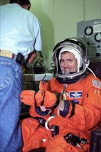 STS-94 Mission Commander James D. Halsell, Jr., puts his left glove on while he is assisted into his launch/entry suit in the Operations and Checkout (O&C) Building