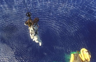 (29 Aug. 1965) --- Astronaut Charles Conrad Jr. is hoisted up to a Navy helicopter while astronaut L. Gordon Cooper Jr. waits in a life raft below after the splashdown of the Gemini-5 spacecraft.