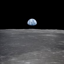 (July 1969) --- This view from the Apollo 11 spacecraft shows the Earth rising above the moon's horizon. The lunar terrain pictured is in the area of Smyth's Sea on the nearside