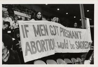 Photograph of women attendees holding a banner reading, "If Men Got Pregnant Abortion Would Be Sacred" at the National Women's Conference, Houston, TX, 11/1977.