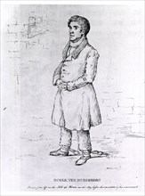 Full length view of Burke, in a prison cell, wearing leg irons.
