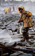 Worker cleaning oil-covered rocks using high-pressure spray in Alaska