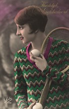 Woman with short hair & sweater with tennis racquet and ball.