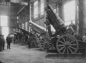 Des mortiers de 260 mm dans un hangar industriel. Des ouvriers posent raides à côté des grandes pièces d'artillerie. c. 1915.