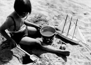 italy, seaside summer camp, little girl playing on the beach, july 1939