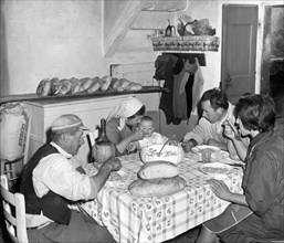 famille à table à l'arrière de la boulangerie, miches de pain toscan sur la table, 1967