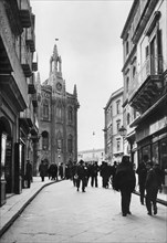 europe, italie, sicile, agrigento, personnes dans la rue avec le bâtiment de la chambre de commerce en arrière-plan, 1934