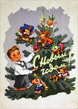 A little boy holds a Christmas tree toy in his hands against the background of a Christmas tree decorated with figurines of fairy tale characters.