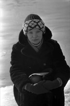 Young woman in a fur coat sitting in the snow.