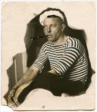 A man in a sailor shirt with a long cigarette holder with a cigarette in his mouth.