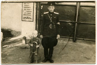 The captain of the Red Army with the boy, who holds the pipe against the gate of the military garrison.