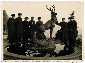 A group of officers on vacation posing near a monument to a deer.