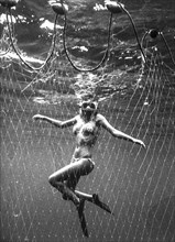 Woman underwater in a fishing net, 70's