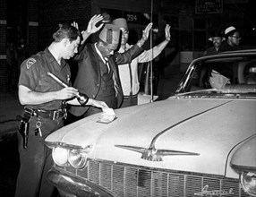 A policeman checks the identification of two negroes after the newark riots, 1967