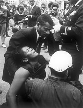 Fainted woman helped by a friend and a police during the funeral march for martin luther king, at lanta, 1968
