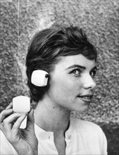 A woman wearing a headset connected to a battery-powered radio, 1959