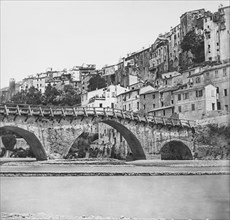A stone arched bridge with wooden handrails surrounded by very old buildings possible Rome.