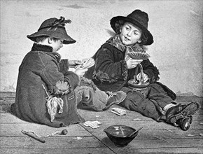 Two young boys playing cards on a boardwalk.