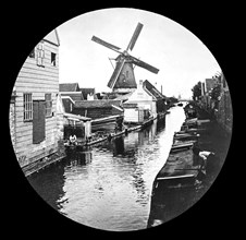 A windmill on the river with old houses and work yards.