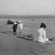 Beach scene with children playing and adults sitting in the sun.