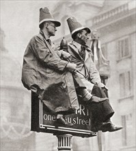 Two men atop a traffic sign in order to get a better view of the Coronation procession of George VI and Queen Elizabeth.