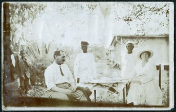 European couple taking tea, attended by African servants