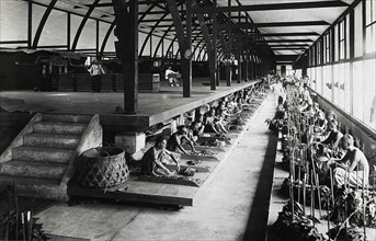 Indian workers sorting tobacco leaves under the supervision of Europeans in a fermentation shed in