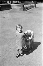 Boy playing with baby carriage for doll, 1938