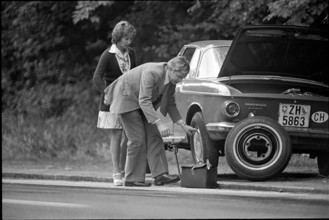 Man helps female driver with flat tire, 1974