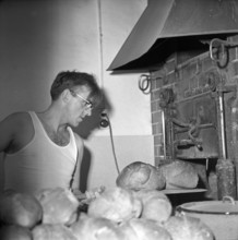 Baker removing loaves of bread from the woodfired oven; 1965