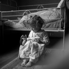 Girl sitting on the floor in front of her bed, Switzerland 1940.