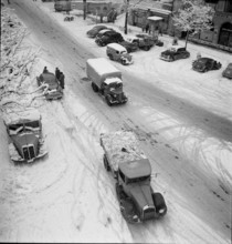 Snowfall in Lausanne: Trucks driving on a snowy street; 1952.