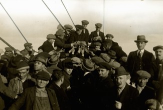 Group of emigrants around the chaplain on the foredeck of the Conte Verde