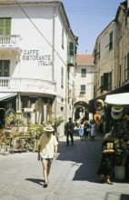 People walking along street, Laigueglia, Savona, Italy, July 1959.