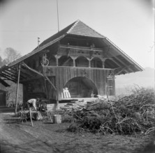 Man bundling firewood in front of a granary in Wynigen BE 1960